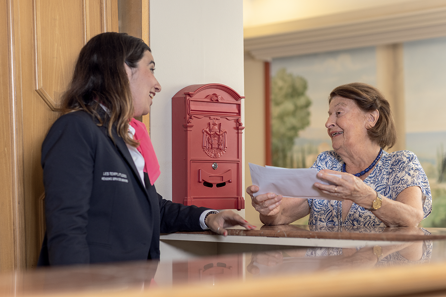 Accueil DomusVi avec une résidente recevant un courrier à la réception de la résidence